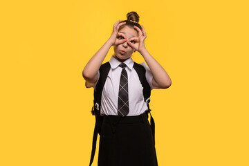 Teen girl making playful glasses gesture with hands, wearing a school uniform and backpack.