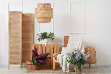 Armchair with plaid and blooming lilac flowers in room