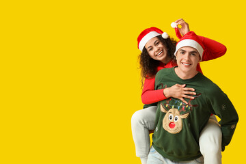 Fototapeta premium Happy young couple in Christmas sweaters having fun on yellow background