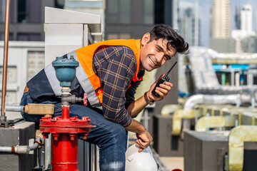 Male technical foreman inspection maintenance sitting on workshop site break relax time with talking on radio call with colleague about plumbing and electrical systems on the roof of a building