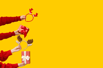 Female hands with Christmas reindeer horns headbands and gift boxes on yellow background
