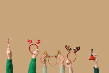 Female hands holding Christmas reindeer horns headbands with bell and candy cane on beige background