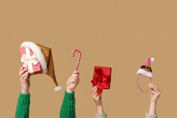 Female hands holding Christmas gift boxes with candy cane and accessories on beige background