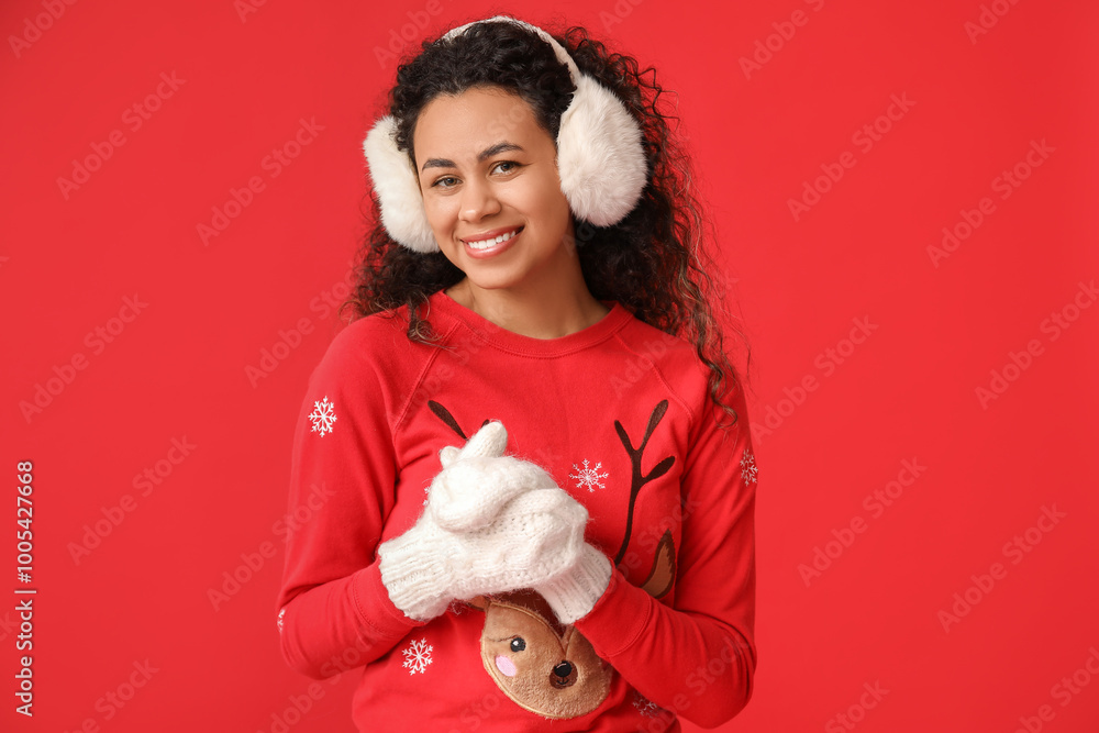 Poster Beautiful young African-American woman in Christmas sweater and warm mittens on red background