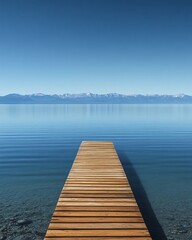 Fototapeta premium A wooden dock extends out into a calm lake with a mountain range in the background.