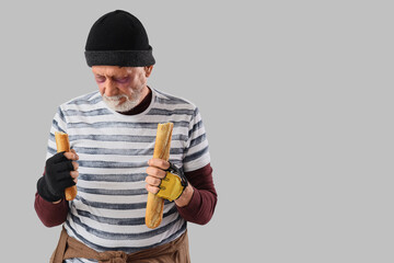 Mature homeless man with baguette on light background