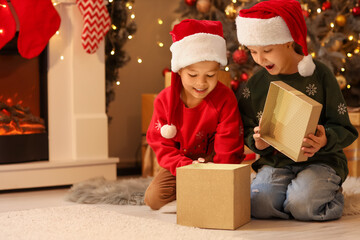Cute happy little children in Santa hats opening gift box on Christmas eve at home