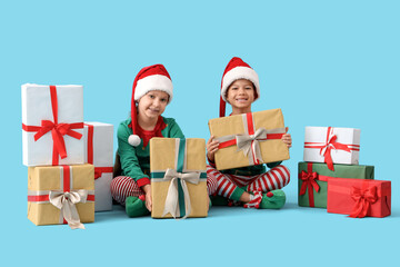 Cute happy little children dressed as elves with Christmas gift boxes sitting on blue background