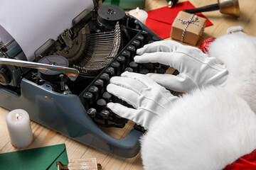 Santa Claus hands with Christmas decor typing on typewriter against beige wooden background