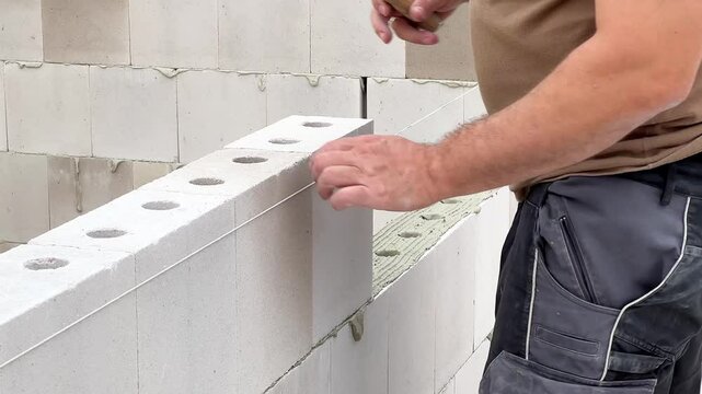 Close up of a construction worker bricklayer laying a wall with white block stones
