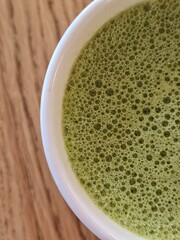 A close-up view of a frothy matcha green tea in a white ceramic cup on a wooden table