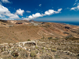 The volcanic landscape of Lanzarote features barren, rugged terrain with layered hills and sparse...