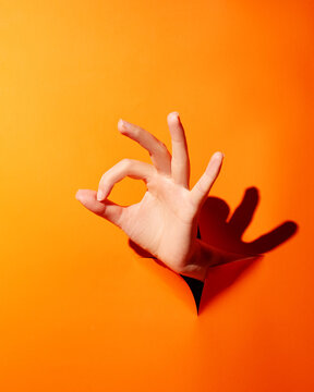 Woman's hand shows ok sign through orange background