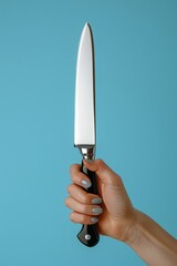 A woman s hand gripping a large black handled kitchen knife against a blue background for text space