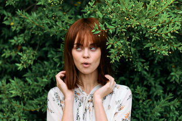 Vibrant redhead woman posing with hands on head in lush green garden setting