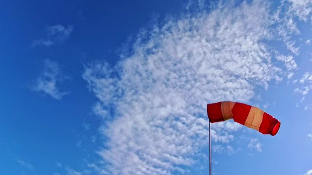leicht im Wind wehende rot-wei&szlig;er Windsack vor blauem leicht bew&ouml;lkten blauem Himmel, Windrichtung, Windgeschwindigkeit, Wetter, Wetterbericht, Luftfahrt, Windrichtungsmesser