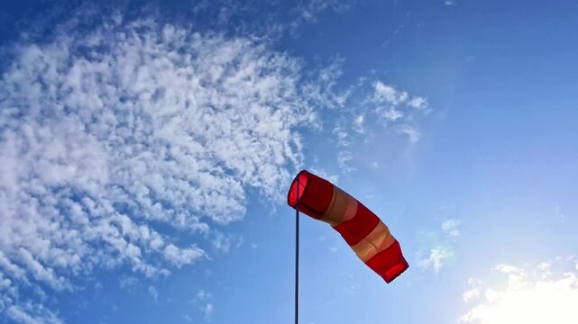 leicht im Wind wehende rot-wei&szlig;er Windsack vor blauem leicht bew&ouml;lkten blauem Himmel, Windrichtung, Windgeschwindigkeit, Wetter, Wetterbericht, Luftfahrt, Windrichtungsmesser