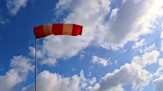 leicht im Wind wehende rot-wei&szlig;er Windsack vor blauem leicht bew&ouml;lkten blauem Himmel, Windrichtung, Windgeschwindigkeit, Wetter, Wetterbericht, Luftfahrt, Windrichtungsmesser