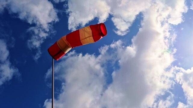 leicht im Wind wehende rot-wei&szlig;er Windsack vor blauem leicht bew&ouml;lkten blauem Himmel, Windrichtung, Windgeschwindigkeit, Wetter, Wetterbericht, Luftfahrt, Windrichtungsmesser