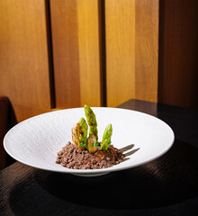 Green asparagus dish served on white plate with brown crumble on black table