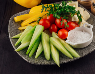 Plate presenting sliced cucumbers, tomatoes, cheese and peppers with spices aside
