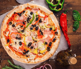 Delicious pizza lying on wooden table surrounded by fresh ingredients