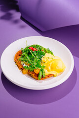 Delicious sweet potato pancakes lying on white plate with salad and sauce on purple background