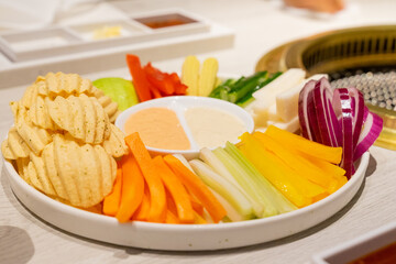A beautifully plated vegetable salad featuring carrots, celery, red and green peppers, crispy potato chips, and refreshing cucumbers sits elegantly on a table at a barbecue restaurant. The vibrant col