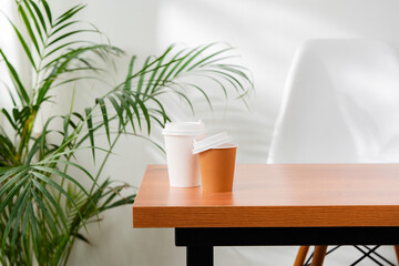 A disposable coffee cup on a wooden table beside a leafy plant