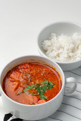 Bowl of curry with pieces of meat and a side of steamed rice arranged neatly for a meal