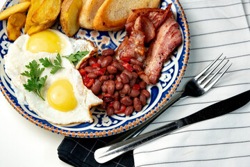 Delicious breakfast plate featuring eggs, beans, bacon, and potato wedges served on a decorative dish