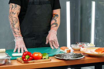 A chef prepares sushi rolls with colorful ingredients on a kitchen counter in a modern cooking space