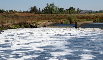 View from below a weir in a river with foam forming on the water