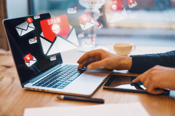 Side view of male hands using laptop on wooden desk with supplies and abstract spam emails on...
