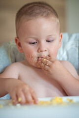 Young child enjoying a messy meal while seated in a high chair during daytime indoors