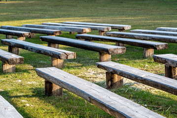 Rows of wooden benches on a green lawn on a sunny summer day