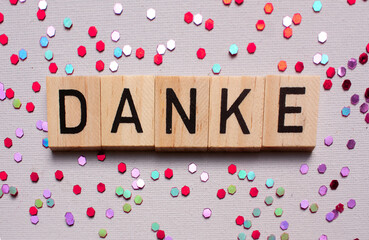 Thank you card with german language DANKE on wooden block on lila background with shiny glitters, panorama