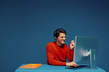 Young man working on computer monitor with headset and eyeglasses