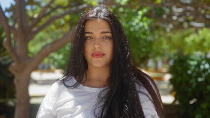 Naklejka premium Woman wearing white shirt posing outdoors with green trees and shrubs in a city park