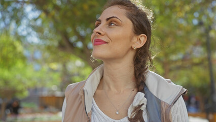 Naklejka premium A contemplative young caucasian woman enjoys the serene ambiance of a lush park outdoors.