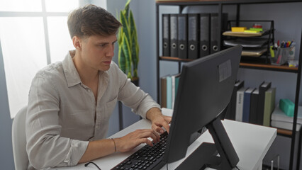 Young man working on a computer in a modern office setting with shelves and plants in the background