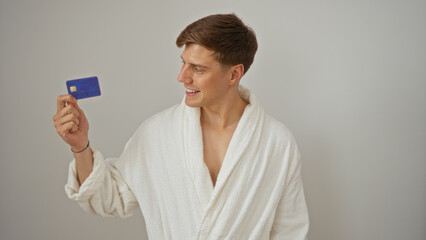 Naklejka premium Young man in a white robe holding and smiling at a credit card, isolated on a white background