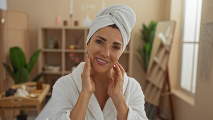 Woman relaxing at a spa salon with a towel on her head and a robe, smiling indoors at a wellness center