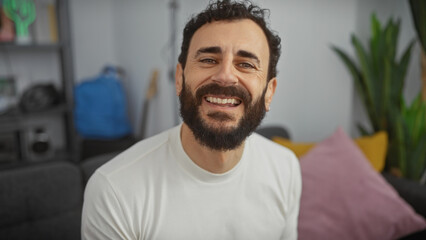 Middle-aged man with beard smiling in a casual modern home interior, exuding warmth and positivity.