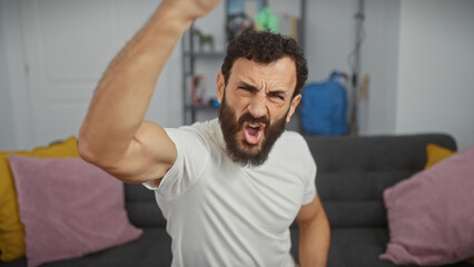 Fist-raising bearded man in white shirt shows excitement in a modern living room.