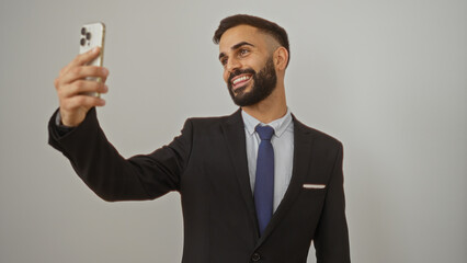 Young man with a beard in a suit taking a selfie over an isolated white background, smiling confidently