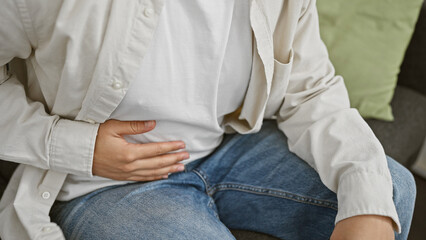 Close-up of a man in a white shirt and jeans sitting on a couch with a green pillow, depicting indoor relaxation or leisure time.