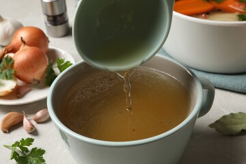 Pouring hot delicious bouillon into cup on light grey table, closeup