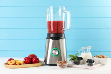 Blender with mixture of ingredients and other fresh products on white wooden table
