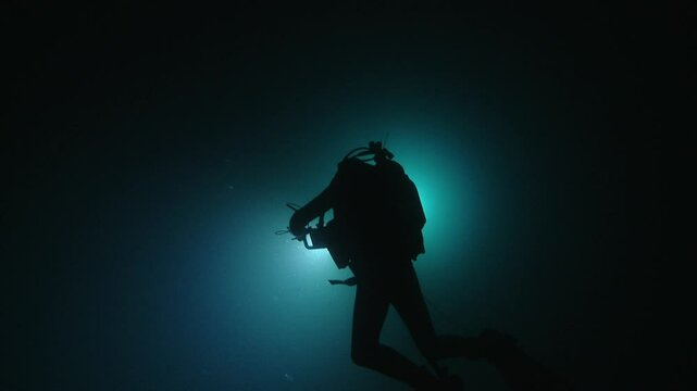 A diver illuminated from behind, creating a silhouette against the dark ocean depths, showcasing the mysterious beauty of the underwater world. Check my portfolio for more ocean footage.